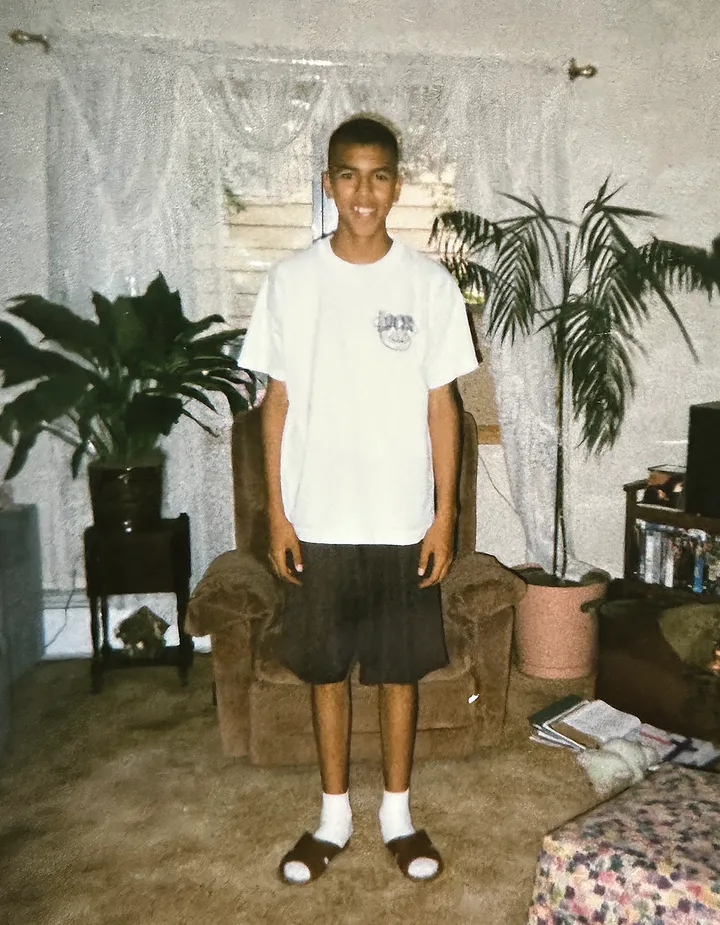 Samuel as a teenager, grinning, standing in his family's living room.